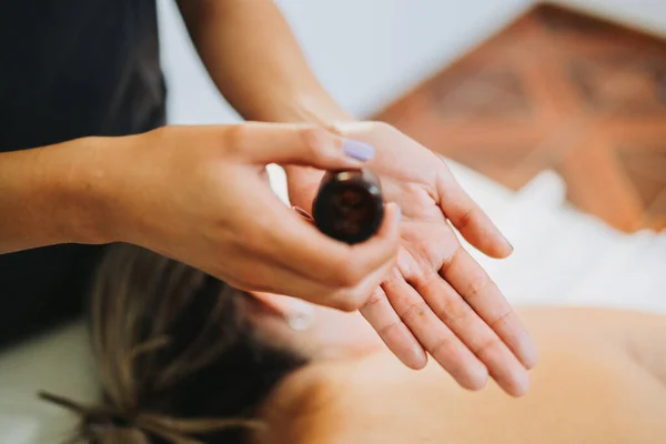Terapeuta irreconocible poniendo aceite de masaje en su mano, para hacer un masaje relajante a una paciente femenina. —  Fotos de Stock