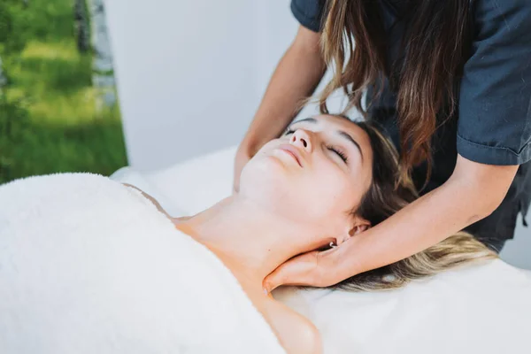 Terapeuta haciendo un masaje en el cuello a una paciente mujer boca arriba. Spa centro de bienestar. Cuidado de la piel. —  Fotos de Stock
