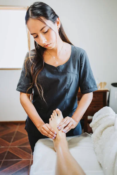 Terapeuta latina haciendo un masaje de pies a una paciente femenina. Spa centro de bienestar. Cuidado de los pies. —  Fotos de Stock