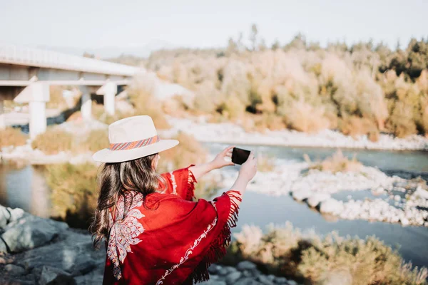 Vibra de verano joven con sombrero y poncho rojo y usando su móvil para tomar fotos en un espacio natural. — Foto de Stock