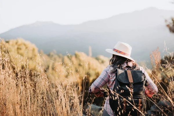 Mujer irreconocible usando un sombrero y con una mochila, haciendo trekking por el campo. — Foto de Stock