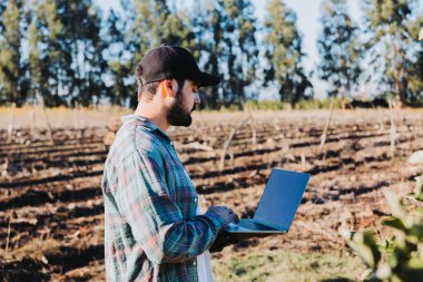 Genç latin çiftçi tarlasının ortasında dizüstü bilgisayarıyla telgraf çekiyor. Tarım sürdürülebilirliği. Kablosuz