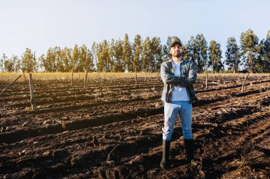 Çiftlik arazisinin ortasında çapraz kollu genç Latin çiftçi. Tarımsal sürdürülebilirlik kavramı.
