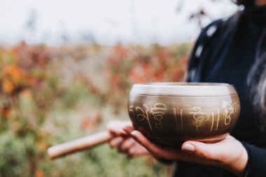 Siyah giyimli kadın elinde ahşap bir kaseyle Tibet şarkı kasesi tutuyor. Seçici odak