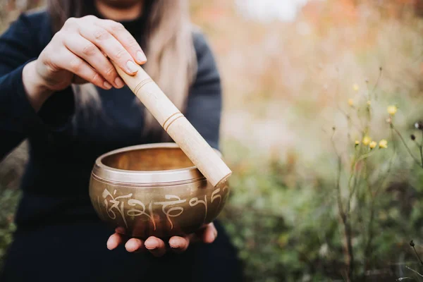 Black dressed woman outside holding and playing a tibetan singing bowl with a wooden stock. Selective focus —  Fotos de Stock