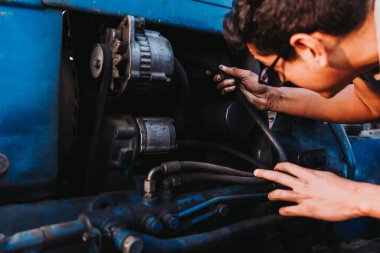 Latin farmer man repairing mechanical problems of an old blue tractor.