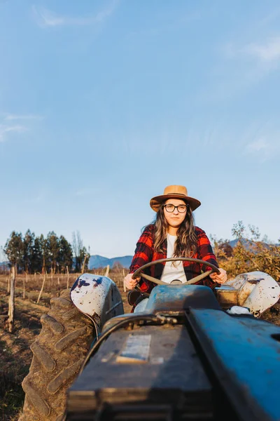 Mujer campesina hispana conduciendo un viejo tractor, en medio de su tierra de cultivo con un cielo azul. — Foto de Stock