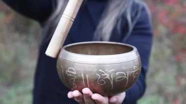 Siyah giyimli Budist kadın, tahta sopayla Tibet kâsesi oynuyor.. 