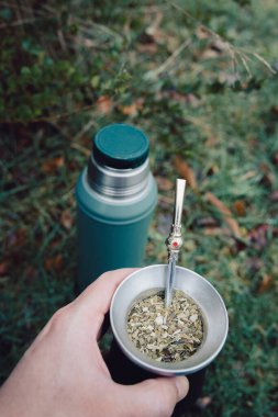 unrecognizable persons hand serving mate with a green thermo, on the green grass. Vertical Latin beverage. Ethnical concept. High quality photo. 