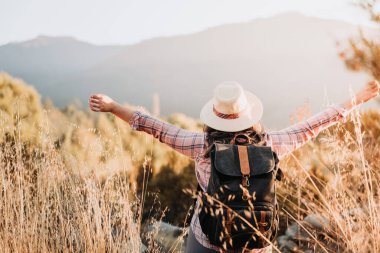 Sırt çantalı tanınmayan bir kadın zafer için kollarını kaldırıyor. Bekar gezgin. Yaz havası. Yüksek kalite fotoğraf. Boşluğu kopyala.
