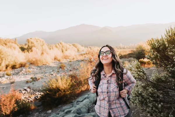Young latin woman with glasses and a backpack on hiking in a beautiful landscape. Summer vibe. High quality photo. Copy space.