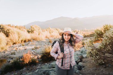 Güzel bir manzarada yürüyüş yapan şapkalı ve sırt çantalı genç Latin bir kadın. Yaz havası. Yüksek kalite fotoğraf. Boşluğu kopyala.