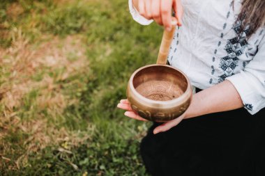 Tanınmayan siyah elbiseli kadın elinde tahta bir sopayla Tibet şarkı kasesi tutuyor..
