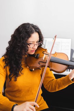 Brunette woman wearing a yellow sweater, and playing violin. High quality photo
