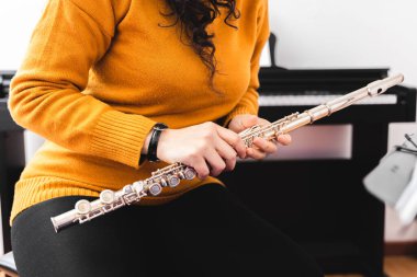 Brunette woman wearing a yellow sweater, and playing a transverse flute. High quality photo