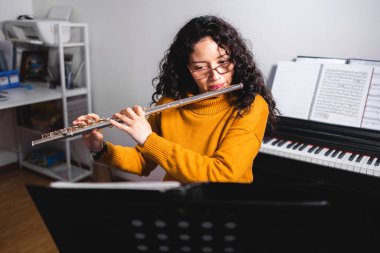 Brunette woman wearing a yellow sweater, and playing a transverse flute. High quality photo