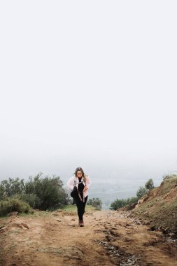 Tired young latin plus size woman with a hat and a backpack on, hiking in a beautiful landscape. High quality photo. Copy space.
