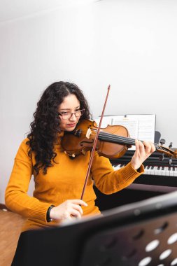 Brunette woman wearing a yellow sweater, and playing violin. High quality photo