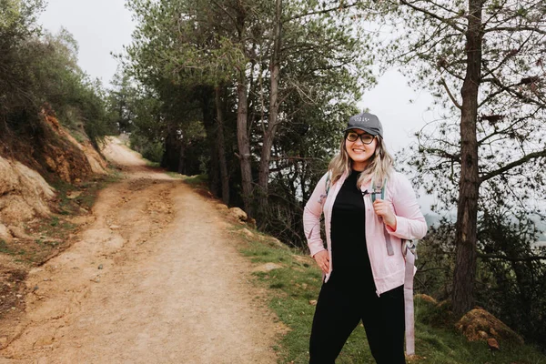 Tired young latin plus size woman with a hat and a backpack on, hiking in a beautiful landscape. High quality photo. Copy space.