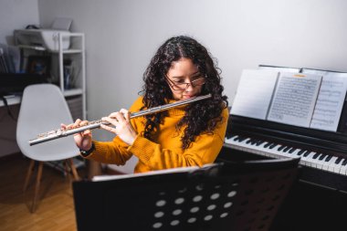 Brunette woman wearing a yellow sweater, and playing a transverse flute. High quality photo