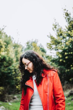 Curly brunette woman, wearing a red leather jacket, and holding a red mug with hot coffee in nature. High quality photo