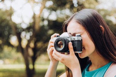 Turkuaz tişört ve sırt çantası giyen, parkta yürürken fotoğraf çeken genç bir turist kadın gezgin. Yüksek kalite fotoğraf