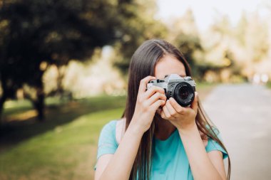 Turkuaz tişört ve sırt çantası giyen, parkta yürürken fotoğraf çeken genç bir turist kadın gezgin. Yüksek kalite fotoğraf