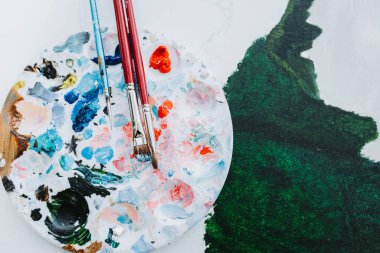 Yuvarlak bir boya paletini kapatır ve yeşil yağlı bir kanvanın üzerine fırçalar. Amatör ressam, kaliteli fotoğraf.