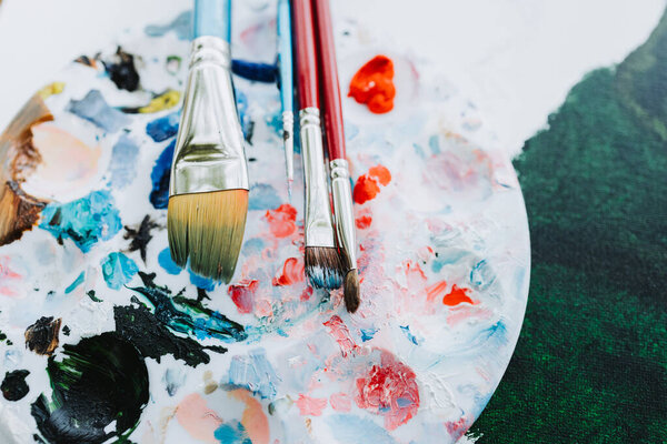 Закрыть круглую палитру красок и наложить кисти на холст, окрашенный зеленым маслом. Высококачественная фотография