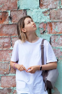 Sırt çantalı bir kız eski bir binadaki kırmızı tuğla duvarın yanında duruyor.