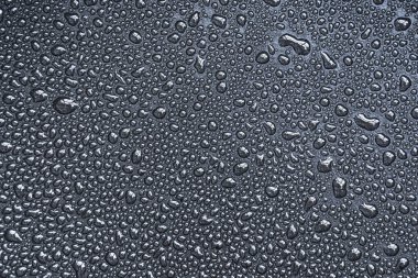 Damlalar, damlalar, damlalar, boncuklar, siyah teflon yüzeyine su damlaları. Tek renkli siyah beyaz makro veya yakın plan arkaplan veya doku