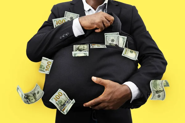 Black Businessman holding black bag full of US dollar notes isolated on white background, money falling from bag
