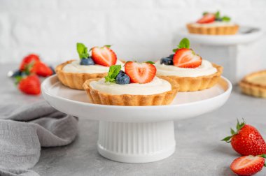 Taze böğürtlenli lezzetli mini tartlar ve gri beton arka planda beyaz bir tabakta krema. Boşluğu kopyala.