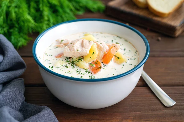Salmon soup with cream, potatoes, carrots and herbs in a bowl on a dark wooden background. Lohikeitto soup. Copy space