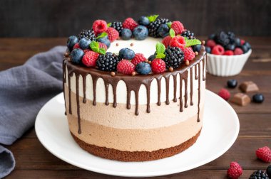 Çikolata jöleli üç çikolatalı kek, yaban mersini, ahududu ve böğürtlen üzerinde siyah ahşap bir arka planda beyaz bir tabakta. Üç farklı tat katmanlı pasta. Boşluğu kopyala