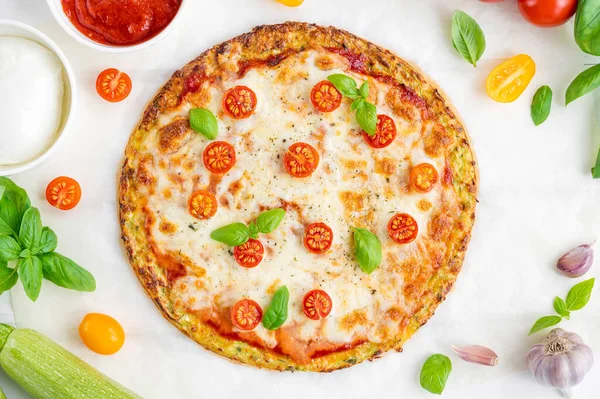 Zucchini crust pizza with tomato sauce, mozzarella cheese, fresh tomatoes and basil on a white wooden background. Zucchini pizza Margarita. Healthy dish