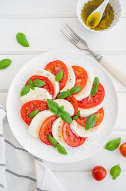 Klasik mozarella peynirli caprese salatası, domates ve fesleğen beyaz bir tabakta ahşap arka planda. Üst görünüm, alanı kopyala