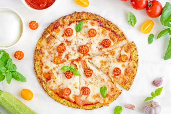 Zucchini crust pizza with tomato sauce, mozzarella cheese, fresh tomatoes and basil on a white wooden background. Zucchini pizza Margarita. Healthy dish