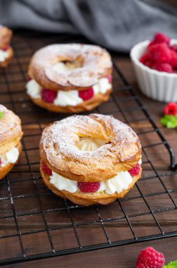 Choux hamur işleri. Krem peynirli Choux halkaları ya da süzme peynir ve ahududu tozu ile kaplanmış koyu ahşap arka planda toz şekeri.