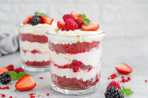 Red Velvet cake trifle with fresh berries in a glass jar on a gray concrete background. Dessert for Valentine's Day. Copy space