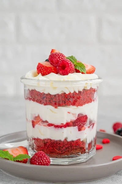 Red Velvet cake trifle with fresh berries in a glass jar on a gray concrete background. Dessert for Valentine\'s Day. Copy space