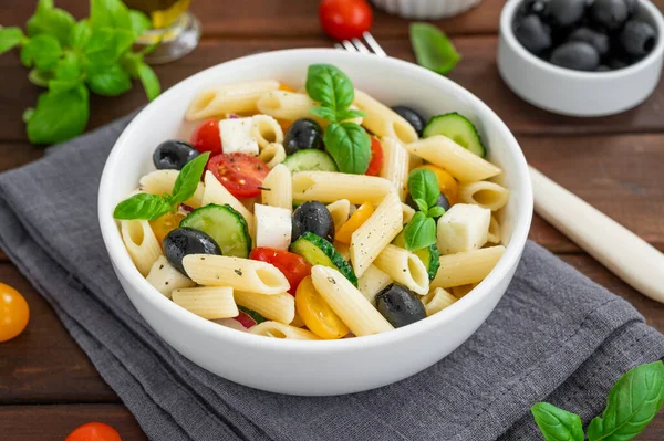 Sağlıklı domatesli makarna salatası, salatalık, kırmızı soğan, zeytin ve peynir koyu ahşap arka planda bir kasede. Boşluğu kopyala