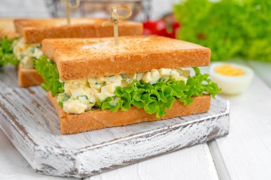 Kızarmış ekmek ve marullu yumurta salatalı sandviç, beyaz ahşap arka planda. Seçici odak.