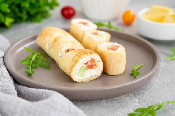 Thin pancake rolls or crepes rolls with smoked salmon, cream cheese, cucumber and dill on a gray concrete background. Selective focus