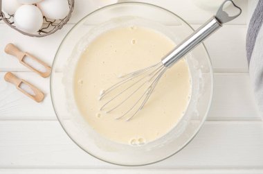 Geleneksel ince krep ya da krep için hamur pişirmek. Yumurta, un, tuz, şeker, süt ve tereyağı beyaz ahşap arka planda bir kasede. Adım adım tarif et. Maslenitsa için yiyecek.