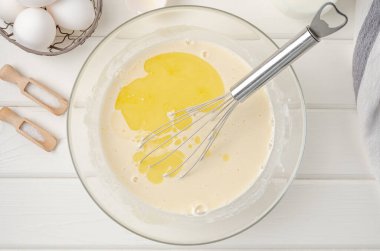 Geleneksel ince krep ya da krep için hamur pişirmek. Yumurta, un, tuz, şeker, süt ve tereyağı beyaz ahşap arka planda bir kasede. Adım adım tarif et. Maslenitsa için yiyecek.