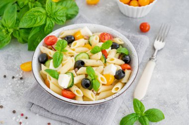 Gri arka planda domatesli, salatalıklı, kırmızı soğanlı, zeytinli ve peynirli sağlıklı makarna salatası. Boşluğu kopyala