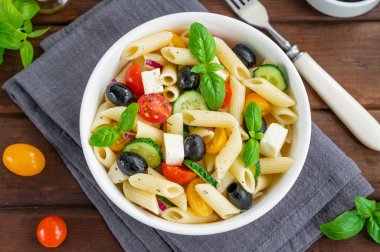 Sağlıklı domatesli makarna salatası, salatalık, kırmızı soğan, zeytin ve peynir koyu ahşap arka planda bir kasede. Boşluğu kopyala