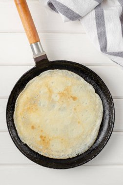 Beyaz ahşap zemin üzerinde geleneksel ince krep ya da krep kızartması. Krepleri ve krepleri adım adım yapma süreci. Maslenitsa için yiyecek.