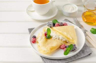 Geleneksel ince krep ya da süzme peynirli krep ve beyaz ahşap arka planda böğürtlen, bal ve ekşi krema. Maslenitsa için yemek. Boşluğu kopyala